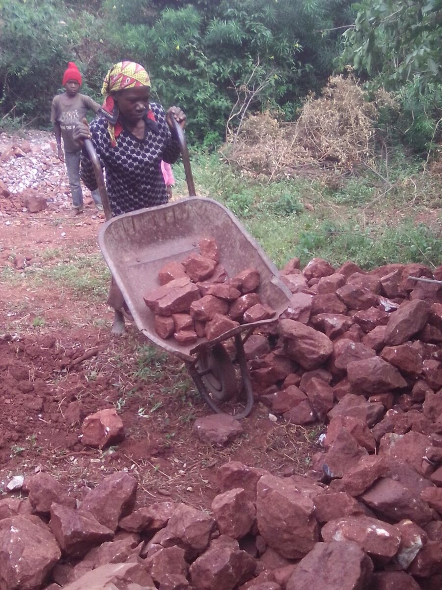 Eunice, Charles Ouma's mother, ferrying stones by wheelbarrow for crushing at the quarry site. They have been struggling to raise fees for their son to no avail, owing to the high cost of living. PHOTO/Gilbert Ochieng, The Scholar Media Africa.